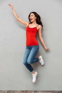 Tam boy görüntü atlama ve uzak gri arka plan üzerinde seyir rahat kıyafetler içinde neşeli esmer kadın