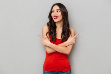 Çapraz silah uzakta gri arka plan üzerinde bakarken taraf için işaret ile rahat kıyafetler mutlu esmer kadın