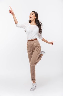 Neşeli bir Asya işkadını ayakta ve beyaz arka plan üzerinde uzak izole parmak işaret tam uzunlukta portresi