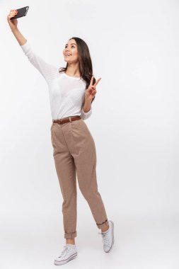 Beyaz arka plan üzerinde izole cep telefonunuzla selfie alarak bir gülümseyen Asya iş kadını tam uzunlukta portresi