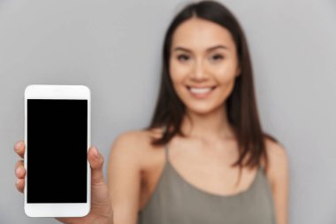 Boş ekran cep telefonu gri arka plan üzerinde izole gösterilen mutlu Asyalı bir kadın portresi