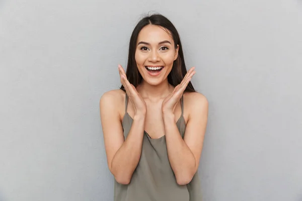 Portrait of an excited asian woman looking at camera and laughing isolated over gray background