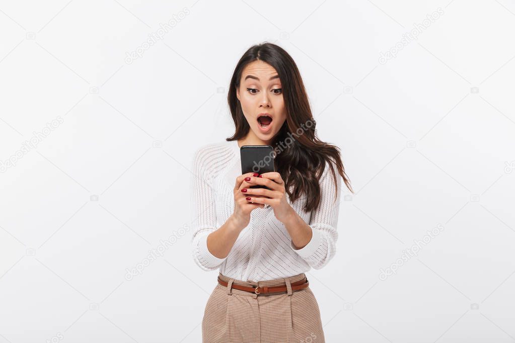 Portrait of a shocked asian businesswoman using mobile phone isolated over white background