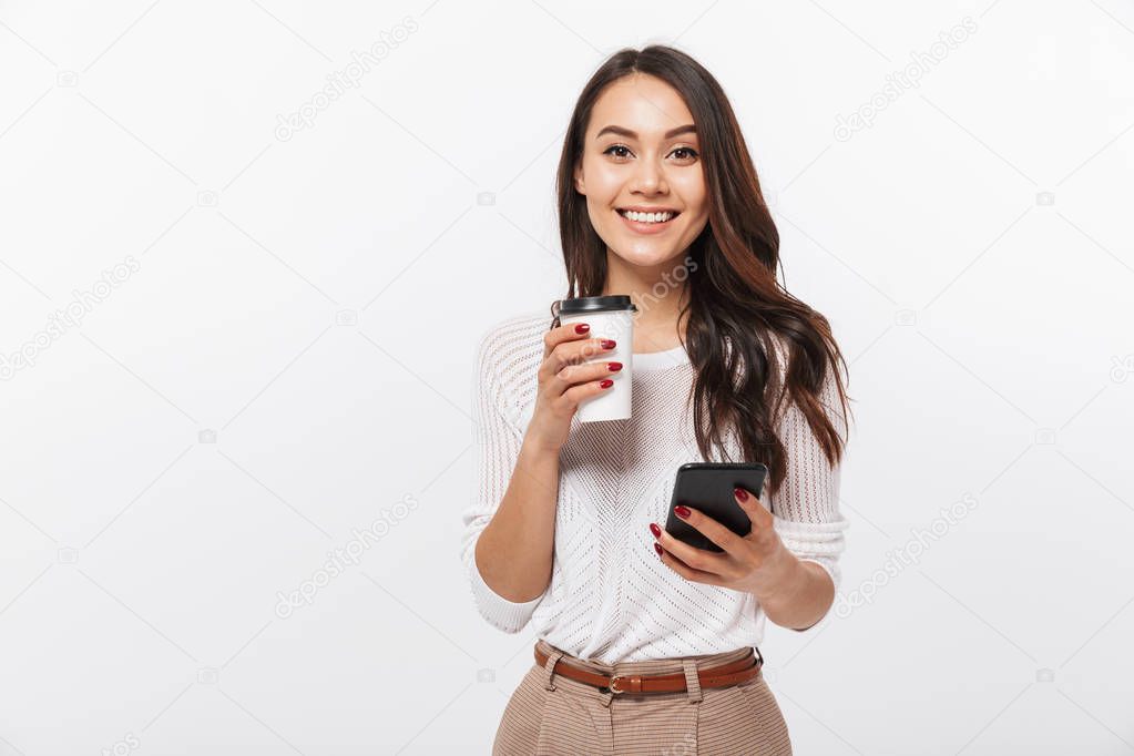 Portrait of a happy asian businesswoman using mobile phone while holding cup of coffee to go isolated over white background