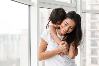 İnanılmaz Aile Anne ve kızı evde büyük pencereler sarılma ederken sevgi ve hassasiyet ifade portresi