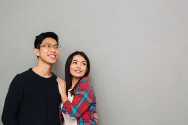 Neşeli Genç Asyalı sevgi dolu çift gri duvar arka plan bir yana bakmaktan izole ayakta.