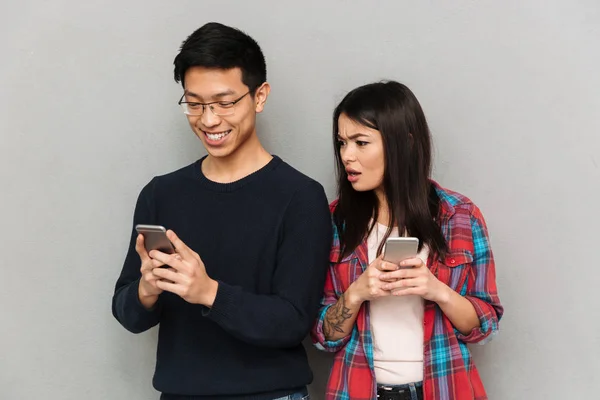 不高兴的形象 年轻的亚洲妇女看着她的男子站在灰色墙上的背景下 手机聊天 — 图库照片