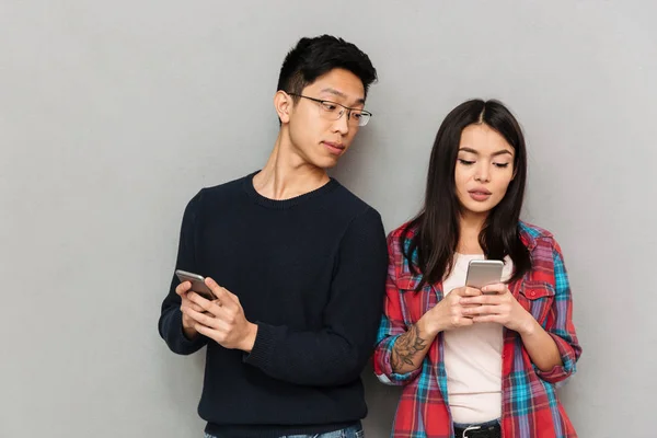 年轻的亚裔男子的形象看着他的女朋友站在灰色墙上的背景下 手机聊天 — 图库照片