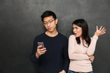 Gözlük onun smartphone dururken memnun kız arkadaşıyla siyah arka plan üzerinde kullanarak memnun Asyalı adam