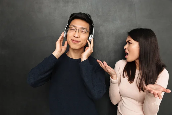 无忧无虑的亚洲人听音乐耳机 而站在他的不满女友在黑色背景附近 — 图库照片