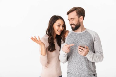 Beyaz arka plan üzerinde izole ayakta heyecanlı genç sevgi dolu çift görüntüsü. Bir kenara cep telefonuyla arıyorsunuz.