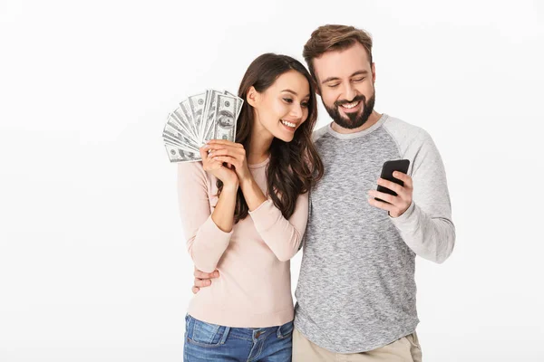 照片的幸福年轻的情侣站在白色背景下 持有钱使用手机 — 图库照片
