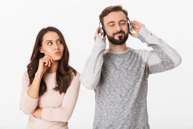 Onun adam ayakta beyaz arka plan kulaklık ile müzik dinleme üzerinde izole bakarak memnun genç kadın görüntüsünü.