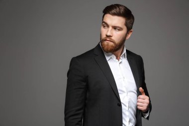Ayakta ve seyir uzağa gri arka plan üzerinde izole ederken kendine güvenen genç işadamı portresi takım elbise poz giyinmiş
