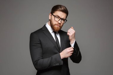 Büyüleyici bir genç işadamı portresi kadar gri arka plan üzerinde izole gömleğinin düğmelerini takım elbise giymiş