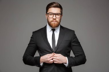 Kendine güvenen genç işadamı portresi kadar gri arka plan üzerinde izole ceketinin düğmelerini takım elbise giymiş