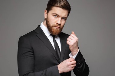 Kendine güvenen genç işadamı portresi kadar gri arka plan üzerinde izole gömleğinin düğmelerini takım elbise giymiş
