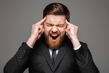 Gri arka plan üzerinde izole onun Tapınağı parmaklar ile takım elbise giymiş bir çığlık atan genç işadamı portresi kapatın