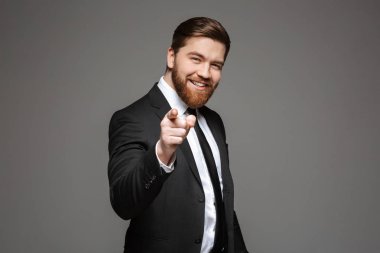 Mutlu bir genç işadamı portresi gri arka plan üzerinde izole kamera, parmak işaret takım elbise giymiş