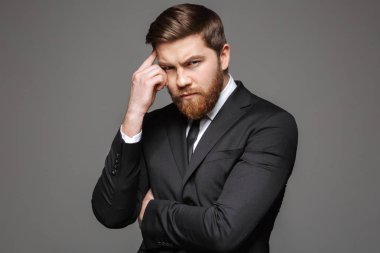 Dalgın bir genç işadamı portresi gri arka plan üzerinde izole kamera bakarak takım elbise giymiş