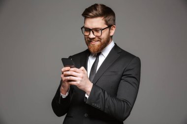 Mutlu bir genç işadamı portresi cep telefonu gri arka plan üzerinde izole kullanarak takım elbise giymiş