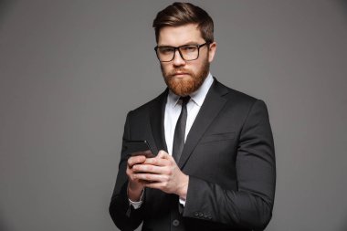 Kendine güvenen genç işadamı portresi cep telefonu gri arka plan üzerinde izole tutan takım elbise giymiş