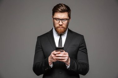 Kendine güvenen genç işadamı portresi cep telefonu gri arka plan üzerinde izole kullanarak takım elbise giymiş