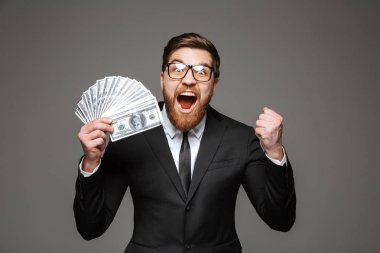 Para banknot gösterilen ve gri arka plan üzerinde izole kutlama takım elbise giymiş bir heyecanlı genç işadamı portresi