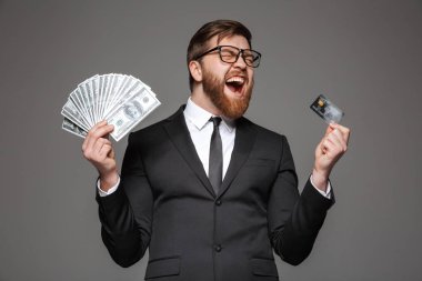 Holding banknot para ve kredi kartı gri arka plan üzerinde izole memnun bir genç işadamı portresi