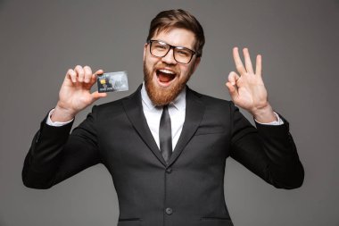 Kredi kartı basılı tutup ok hareket izole gri arka plan üzerinde gösterilen mutlu bir genç işadamı portresi