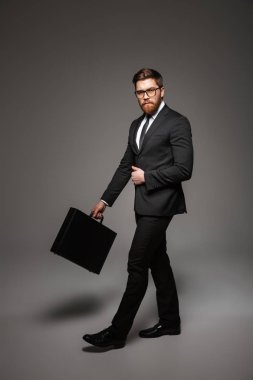Kendine güvenen genç işadamı portresi tam uzunlukta gri arka plan üzerinde izole evrak çantası ile yürüme takım elbise giymiş