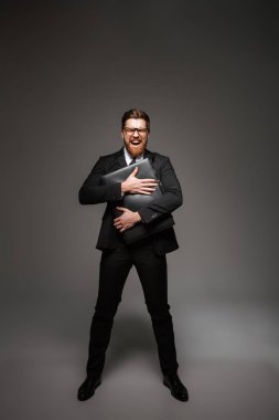 Heyecanlı bir genç işadamı portresi tam uzunlukta evrak çantası gri arka plan üzerinde izole tutan takım elbise giymiş