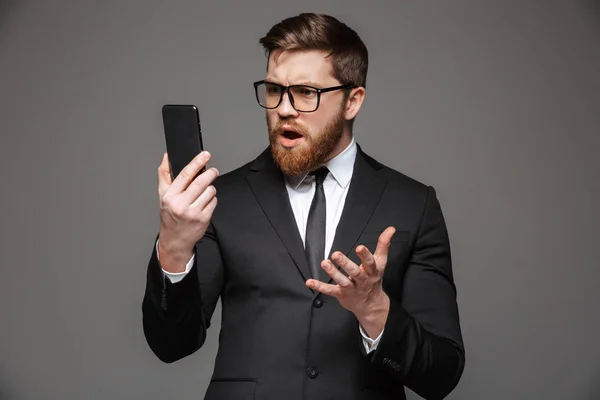 Portret Mylić Młody Biznesmen Ubrany Garnitur Patrząc Telefon Komórkowy Białym — Zdjęcie stockowe