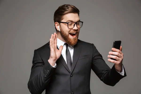 一个快乐的年轻商人的肖像挥舞着手机在灰色背景下被孤立的手机 — 图库照片