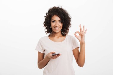 Smartphone kullanarak ve ok sembolü beyaz arka plan üzerinde izole gösterilen t-shirt giyen afro saç modeli ile neşeli esmer kadın