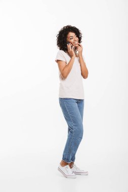 T-shirt ve kot pantolon beyaz arka plan üzerinde izole zevk ile cep telefonuyla konuşan afro saç modeli ile içerik Amerikan kadın tam uzunlukta resim