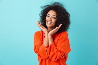 Çekici kadın gülümseme ile fotoğraf makinesinde seyir ve mavi arka plan üzerinde izole yüzünü ellerini tutarak renkli gömlek