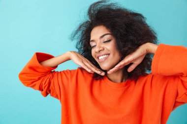 Gülümseme ile fotoğraf makinesinde seyir ve mavi arka plan üzerinde izole yüzünü ellerini tutarak turuncu gömlekli güzel pozitif kadın