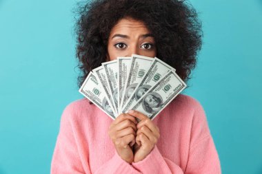Heyecanlı kadın 20'li yaşlarda para dolar faturaları üzerinde mavi arka plan izole hayranı ile yüz kapsayan afro saç modeli ile portresi