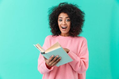Mutlu kadın 20'li yaşlarda heyecan ve holding kitap üzerinde mavi arka plan izole elinde kamera seyir afro saç modeli ile görüntü