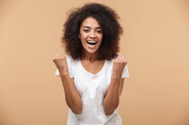 Bej renkli arka plan üzerinde izole başarı kutluyor neşeli bir genç Afrikalı kadın portresi