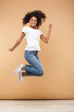 Heyecanlı bir genç Afrikalı kadın atlama izole bej renkli arka plan üzerinde iken başarı kutluyor tam uzunlukta portresi