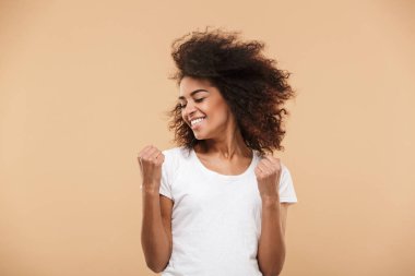 Bej renkli arka plan üzerinde izole başarı kutluyor bir heyecanlı genç Afrikalı kadın portresi