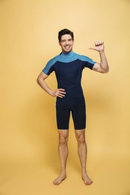 Neşeli bir genç adam görüntüsünü kendisine işaret eden sarı arka plan üzerinde izole mayo giymiş.