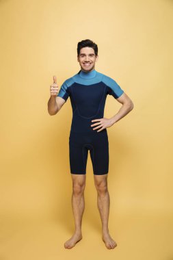 Neşeli bir genç adam görüntüsünü başparmak gösterilen sarı arka plan üzerinde izole mayo giymiş.