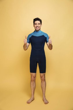 Neşeli bir genç adam görüntüsünü başparmak gösterilen sarı arka plan üzerinde izole mayo giymiş.