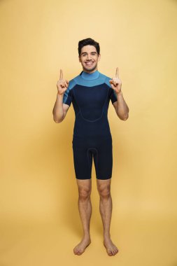 Fotoğraf genç gülümseyen bir adam boşaltmak işaret gösterilen sarı arka plan üzerinde izole mayo giymiş.