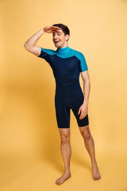 Uzakta izole sarı arka plan üzerinde mayo bakarak mutlu bir genç adam portresi tam uzunlukta giyinmiş