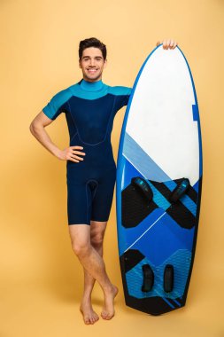 Neşeli bir genç adam portresi sarı arka plan üzerinde izole surfboard holding mayo giymiş.