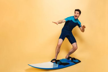 Neşeli bir genç adam portresi tam uzunlukta sarı arka plan üzerinde izole bir tahta üzerinde sörf mayo giymiş